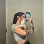 person, cat, mirror, selfie, kitten, tattoos, phone, smartphone, bracelet, bathroom, mirror_selfie, door, light_switch, wall, crop_top, pigtails, reflection, holding, portrait, home_interior