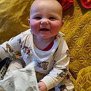 Bradley joined the competition — help win amazing prizes! baby, child, pajamas, smiling, sitting, blanket, yellow, face, hands, footwear, socks, toy, remote_control, indoor, cute, infant, playful, happy, comfort, soft
