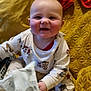 baby, child, pajamas, smiling, sitting, blanket, yellow, face, hands, footwear, socks, toy, remote_control, indoor, cute, infant, playful, happy, comfort, soft