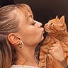woman, cat, orange_cat, kiss, face, earrings, indoor, portrait, pet, affection, hair, holding, cute, feline, expression, animal, young_adult, casual, love, closeup
