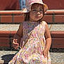 child, girl, floral_dress, sun_hat, outdoor, steps, tiled_floor, sunlight, shadow, sitting, portrait, young_child, casual_clothing, daylight, cute, summer, fashion, person, background_blur, expression