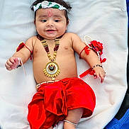 Daivik is registered to the contest to win money with this photo: baby, child, smiling, traditional_clothing, red_skirt, jewelry, bracelet, headband, peacock_feather, lying_down, blanket, cute, happy, infant, anklet, cultural, portrait, indoors, decorative, celebration