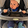 Zion is registered to the contest to win money with this photo: baby, child, stroller, graco, cap, hat, blue_clothing, striped_socks, hands, face, eyes, infant, seat, baby_tray, curious, portrait, indoor, cute, expression, young_child