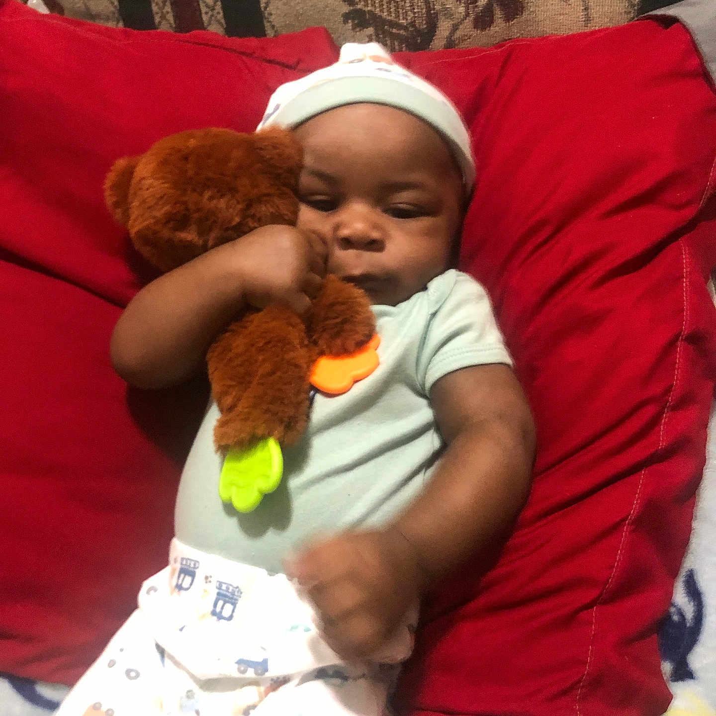 Keison joined the competition — help win amazing prizes! baby, baby_clothes, bed, blanket, brown_skin, child, cozy, cuddling, face, indoors, infant, onesie, pacifier, photograph, portrait, red_pillow, seated, sleepy, teddy_bear, toy