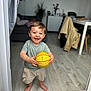 Mathéo a rejoint le concours — aidez-le/la à gagner de superbes lots ! barefoot, basketball, casual_clothing, child, coat, furniture, happy, home, indoor, living_room, modern, person, plant, portrait, shorts, smiling, toddler, toy, tshirt, wooden_floor