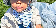 Mathéo a rejoint le concours — aidez-le/la à gagner de superbes lots ! baby, bib, blanket, casual_clothing, child, curious, cute, daylight, denim_overalls, footwear, grass, hat, outdoor, portrait, shoe, sitting, striped_hat, sunlight, toddler, white_jacket