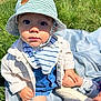 baby, bib, blanket, casual_clothing, child, curious, cute, daylight, denim_overalls, footwear, grass, hat, outdoor, portrait, shoe, sitting, striped_hat, sunlight, toddler, white_jacket