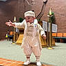 toddler, child, ceremonial_clothing, church, indoor, smiling, standing, brick, carpet, hat, formal_wear, religious, cross, altar, decor, person, white_shoes, gesture, happy, celebration