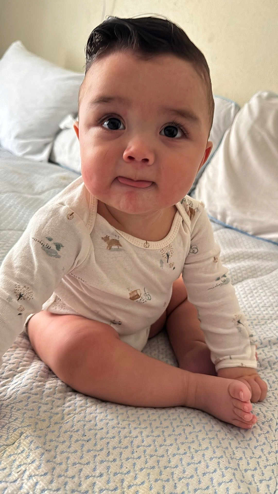 Emiliano is registered to the contest to win money with this photo: baby, infant, child, onesie, bed, blanket, pillow, tongue, cute, skin, face, eyes, hand, foot, sitting, indoors, soft_lighting, expression, portrait, home
