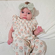 Hazel is registered to the contest to win money with this photo: baby, infant, headband, bow, floral_outfit, sitting, white_background, cute, portrait, indoors, child, foot, hand, pink_skin, wide_eyes, quilted_surface, timestamp, day_overlay, curious_expression, soft_lighting