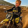Samuel is registered to the contest to win money with this photo: child, dirt_bike, motocross, racing, outdoor, helmetless, dirt_track, yellow_clothing, black_clothing, blonde_hair, young_boy, motorcycle, sport, dust, sunny, blue_sky, hill, action, gloves, boots