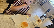 Samuel is registered to the contest to win money with this photo: child, toddler, curly_hair, striped_shirt, eating, restaurant, table, chair, bread, dipping_sauce, drink, phone, video, indoor, tile_floor, window, bench, napkin, food, meal
