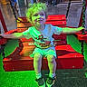 Samuel is registered to the contest to win money with this photo: child, swing, red_swing, curly_hair, green_light, indoor, casual_clothing, spiderman_shirt, sneakers, happy, smiling, playing, seated, people_in_background, floor_tiles, table, chairs, adult, public_space, fun
