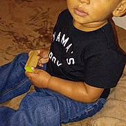 Dominic joined the competition — help win amazing prizes! child, toddler, indoor, sitting, brown_blanket, black_tshirt, blue_jeans, curious, holding_object, young_child, casual_clothing, cozy, portrait, face, person, home, furniture, relaxed, young, cute