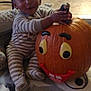 child, toddler, pumpkin, jack_o_lantern, striped_pajamas, sitting, smile, indoors, carpet, living_room, blanket, hand, face, happy, toy, floor, home_interior, holiday_decor, playtime, cute