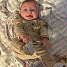 baby, infant, smiling, onesie, headband, blanket, striped, toy, playful, cute, lying_down, cozy, soft, child, person, indoors, happy, clothing, footwear, portrait