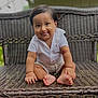baby, child, smiling, tongue_out, sitting, wicker_bench, outdoor, grass, white_shirt, cute, portrait, happy, infant, person, funny_face, short_hair, natural_light, skin, expression, casual_clothing