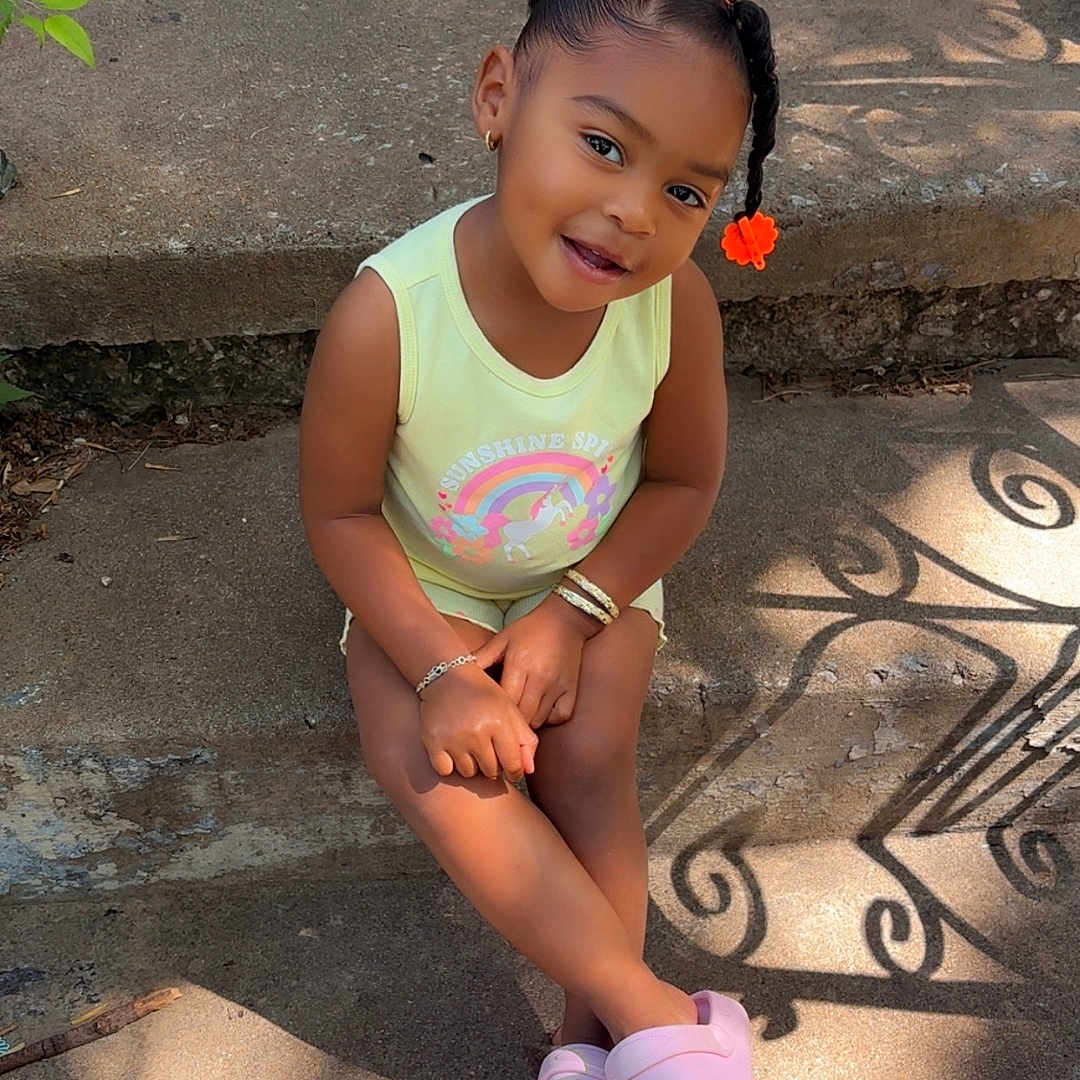 Alanna joined the competition — help win amazing prizes! bracelet, casual_clothing, child, concrete, cute, daylight, hair_accessory, happy, outdoor, pink_slippers, portrait, rainbow_print, shadow, sitting, smiling, steps, sunlight, toddler, yellow_shirt, young_girl