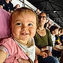 baby, smiling, child, person, crowd, audience, indoor, stadium, glasses, woman, holding, clothing, bib, hand, face, happy, people, seated, event, casual