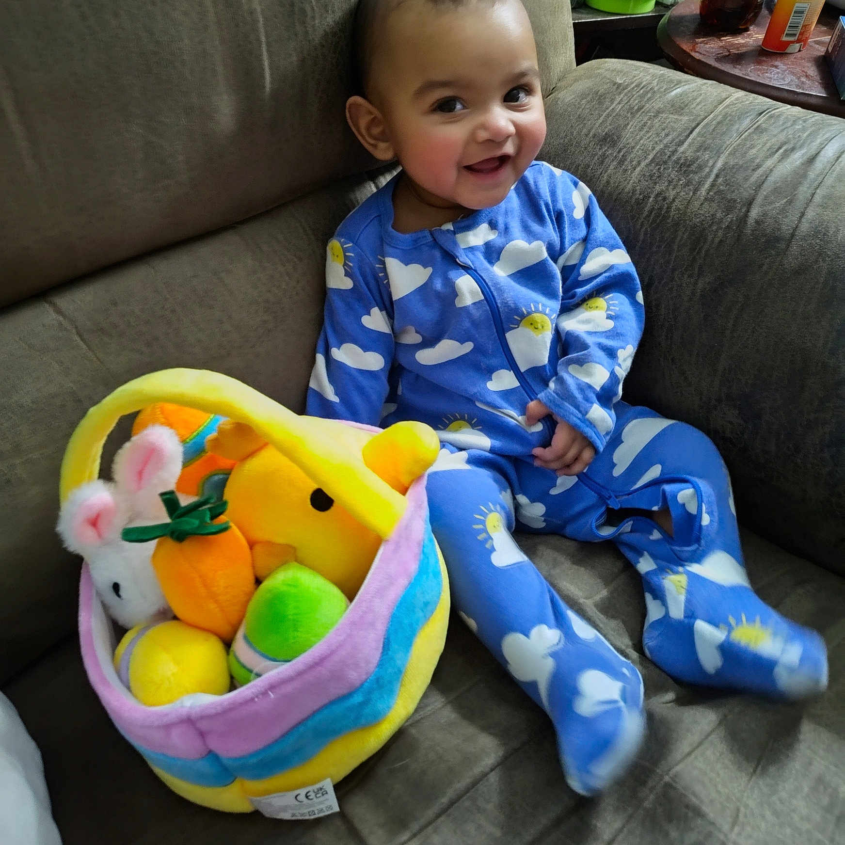 Miracle joined the competition — help win amazing prizes! baby, child, smiling, blue_pajamas, cloud_pattern, plush_toys, easter_basket, couch, indoor, cute, happy, person, toy, soft_toys, seated, infant, home, colorful, face, cozy