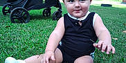 Ace is registered to the contest to win money with this photo: baby, black_clothing, child, curly_hair, daylight, grass, greenery, lawn, nature, outdoor, park, person, playful, sitting, smile, stroller, toddler, trees, white_shoes, young_child