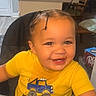 Zaylin is registered to the contest to win money with this photo: toddler, child, high_chair, yellow_shirt, braided_hair, smiling, food_crumbs, kitchen, indoor, table, chair, face, person, happy, eating, furniture, appliance, home, baby, tray