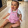 baby, child, pink_overalls, white_shirt, hair_bow, pigtails, wooden_floor, door, indoor, smiling, sitting, cute, happy, person, flooring, home_interior, jacket, coat, furniture, playful