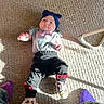 baby, bows, carpet, casual, child, clothing, floor, headband, home_interior, indoor, infant, laying_down, pants, person, purple_socks, shirt, shoes, sunlight, texture, toddler
