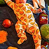 baby, toddler, onesie, taco_print, towel, tomato, onion, yellow_bell_pepper, green_bell_pepper, shredded_cheese, taco_sauce, picante_sauce, lettuce, tortillas, food, smiling, lying_down, indoor, cute, infant