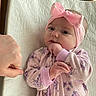 baby, baby_girl, child, closeup, cute, fist_bump, floral_pattern, hand, headband, indoors, infant, lying_down, pajamas, person, pink_bow, portrait, quilted_blanket, sleepwear, soft_lighting, wooden_furniture