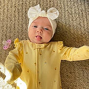 Nala joined the competition — help win amazing prizes! baby, infant, child, headband, bow, yellow_onesie, carpet, pacifier, tongue_out, cute, playful, indoor, soft_light, texture, lying_down, cozy, adorable, smiling, person, young_child