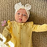 baby, infant, child, headband, bow, yellow_onesie, carpet, pacifier, tongue_out, cute, playful, indoor, soft_light, texture, lying_down, cozy, adorable, smiling, person, young_child