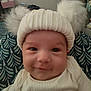 baby, child, hat, knit_hat, pom_poms, smile, face, infant, cozy, white_clothing, cushion, pattern, indoor, portrait, cute, young_child, warm, comfort, headwear, happy