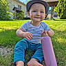 Augustin a rejoint le concours — aidez-le/la à gagner de superbes lots ! toddler, child, hat, blue_pants, barefoot, grass, water_bottle, outdoor, sunny, smile, house, greenery, garden, daylight, person, nature, happy, casual_clothing, sitting, playful