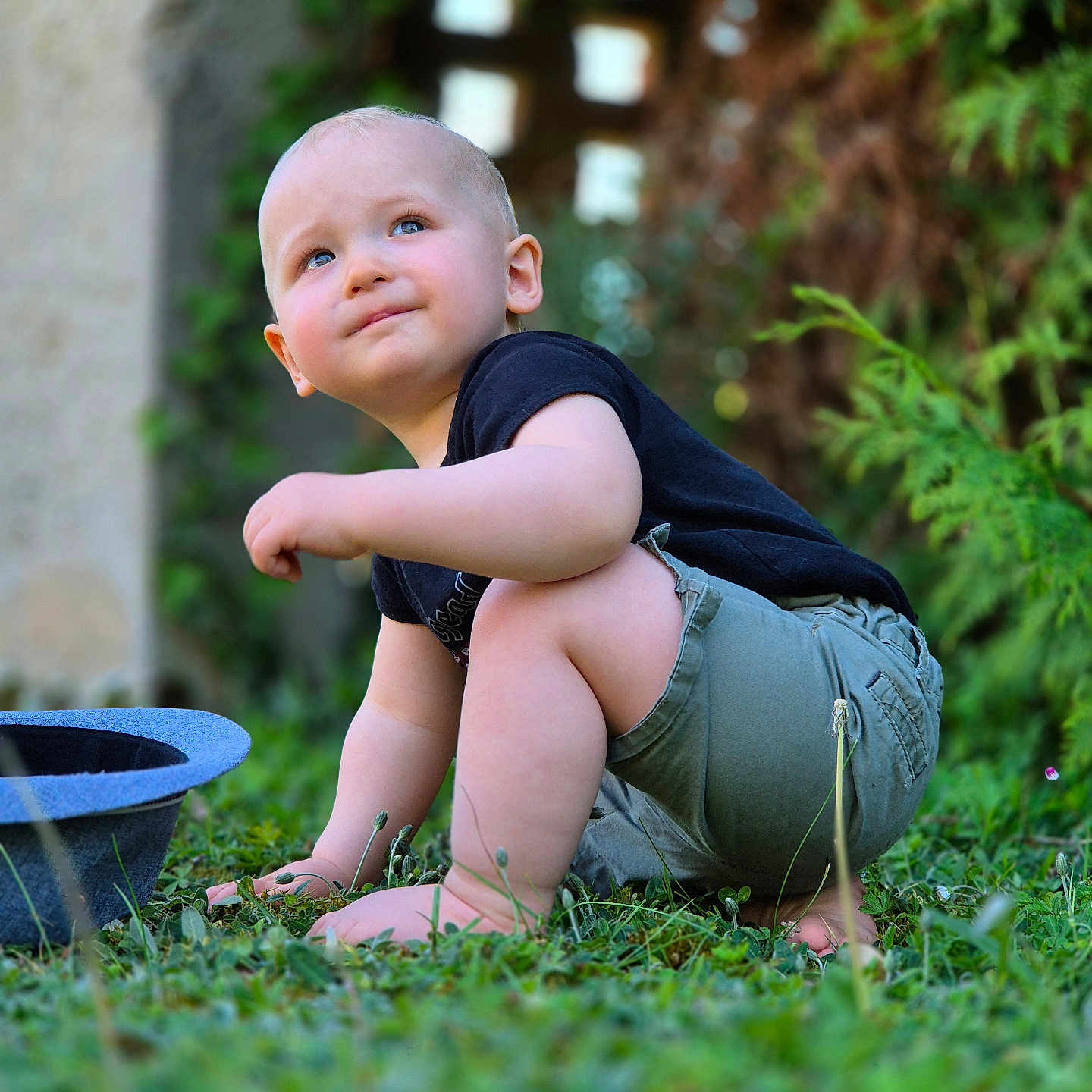 Augustin participe au concours pour gagner de l'argent avec cette photo : toddler, child, grass, outdoor, greenery, hat, cute, portrait, baby, summer, nature, sitting, casual_clothing, shorts, black_shirt, garden, curious, daylight, young, barefoot