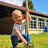 toddler, child, outdoor, grass, garden_tool, blue_sky, clouds, building, window, sunny, casual_clothing, jeans, short_sleeve_shirt, greenery, daytime, playful, crouching, nature, young_child, summer