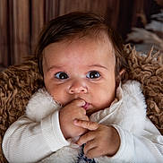 Julia a rejoint le concours — aidez-le/la à gagner de superbes lots ! baby, infant, face, hand, fingers, white_clothing, fur_blanket, brown_background, curious, cute, portrait, indoor, child, young, expression, cozy, soft_texture, closeup, person, warm