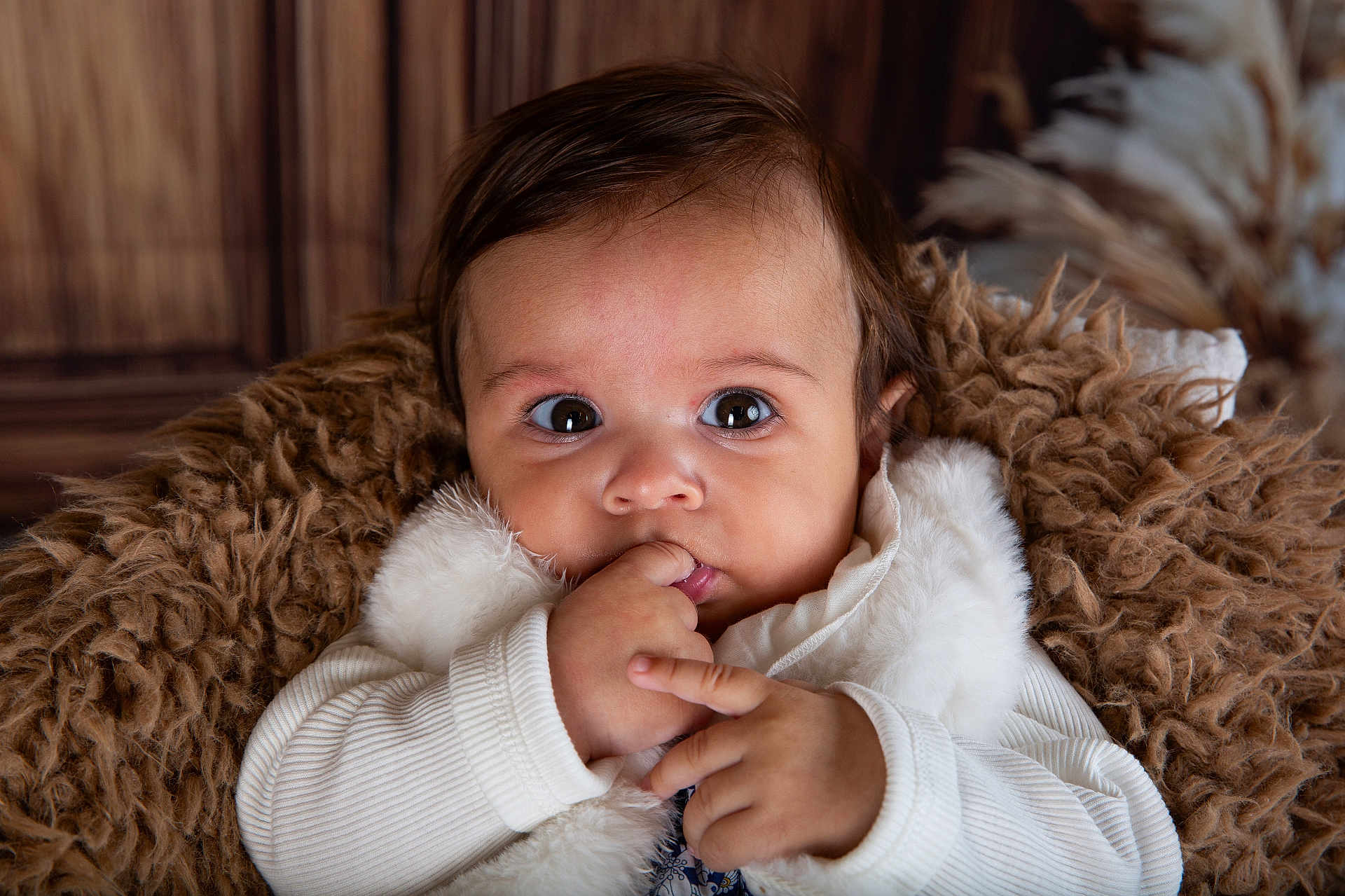 Julia a rejoint le concours — aidez-le/la à gagner de superbes lots ! baby, infant, face, hand, fingers, white_clothing, fur_blanket, brown_background, curious, cute, portrait, indoor, child, young, expression, cozy, soft_texture, closeup, person, warm