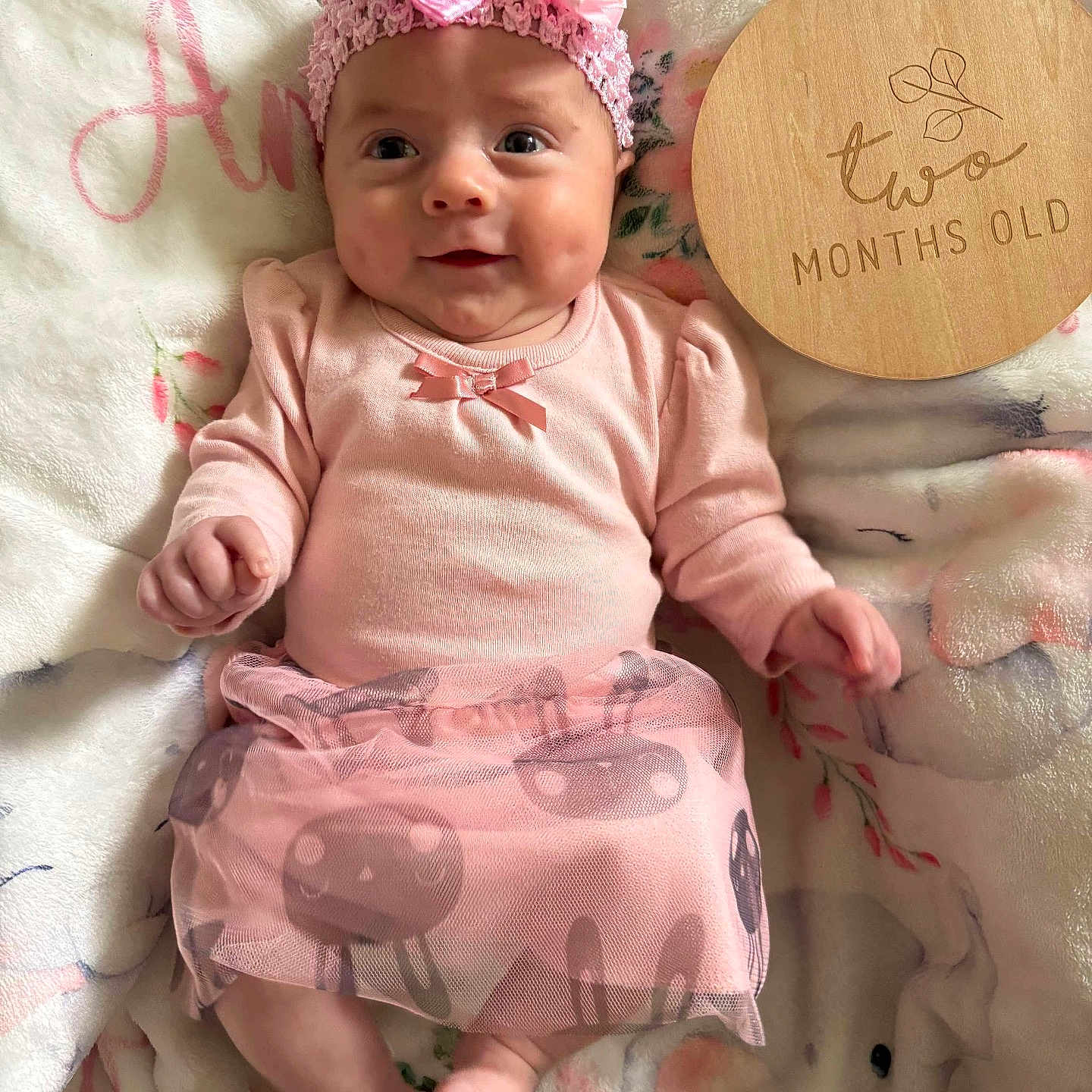 Amani joined the competition — help win amazing prizes! adorable, baby, baby_girl, blanket, child, cute, footwearless, headband, indoors, infant, lying_down, milestone, pastel_colors, pink_clothing, portrait, skirt, smiling, soft_texture, two_months_old, wooden_plaque