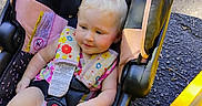 Emery joined the competition — help win amazing prizes! baby, blonde_hair, car_seat, child, clothing, colorful, curb, foot, happy, infant, outdoor, person, road, safety_harness, seatbelt, sitting, smiling, sunlight, yellow_paint, young_child