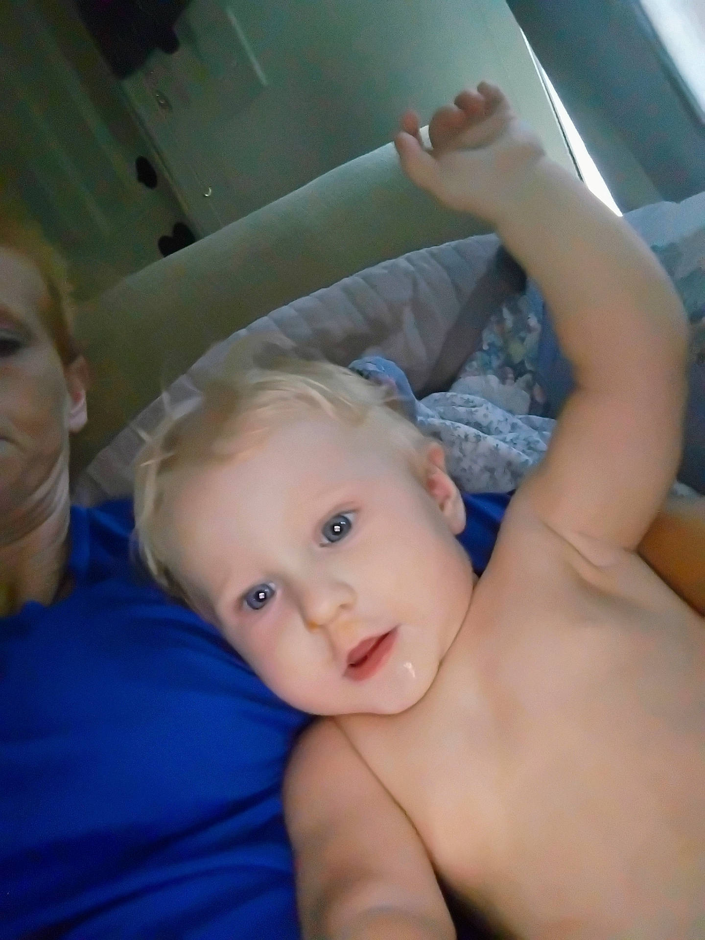 Emery is registered to the contest to win money with this photo: adult, arm, blanket, blonde_hair, blue_eyes, casual, child, closeup, couch, curious, face, family, home, indoor, person, portrait, raising_arm, relaxed, shirt, toddler