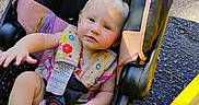 Emery is registered to the contest to win money with this photo: baby, blonde_hair, car_seat, child, clothing, colorful, cute, foot, hand, harness, infant, outdoor, pavement, person, safety, seat_belt, sitting, striped, sunlight, yellow_curb