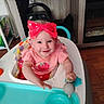 baby, child, cute, face, fireplace, furniture, happy, headwear, high_chair, home, indoor, infant, person, pink_clothing, red_bow, seat, smiling, table, toy, wooden_floor