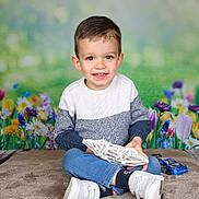 Naïm participe au concours pour gagner de l'argent avec cette photo : child, boy, smiling, sweater, jeans, white_shoes, toy_car, flower_background, indoor, portrait, cross_legged, holding_object, happy, cute, young, casual_clothing, colorful, decorative, playful, studio