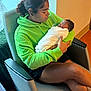 Kashmir is registered to the contest to win money with this photo: woman, newborn, baby, holding, chair, green_hoodie, indoor, peaceful, sleeping, person, blanket, seated, hair, skin, window, natural_light, comfort, tenderness, portrait, casual_clothing