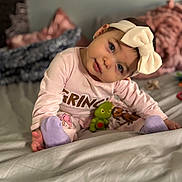 Azariah joined the competition — help win amazing prizes! baby, bed, blanket, bow, child, cozy, curious, cute, headband, indoor, person, pillow, pink_clothing, plush_toy, portrait, purple_socks, sitting, soft_focus, toddler, young_child