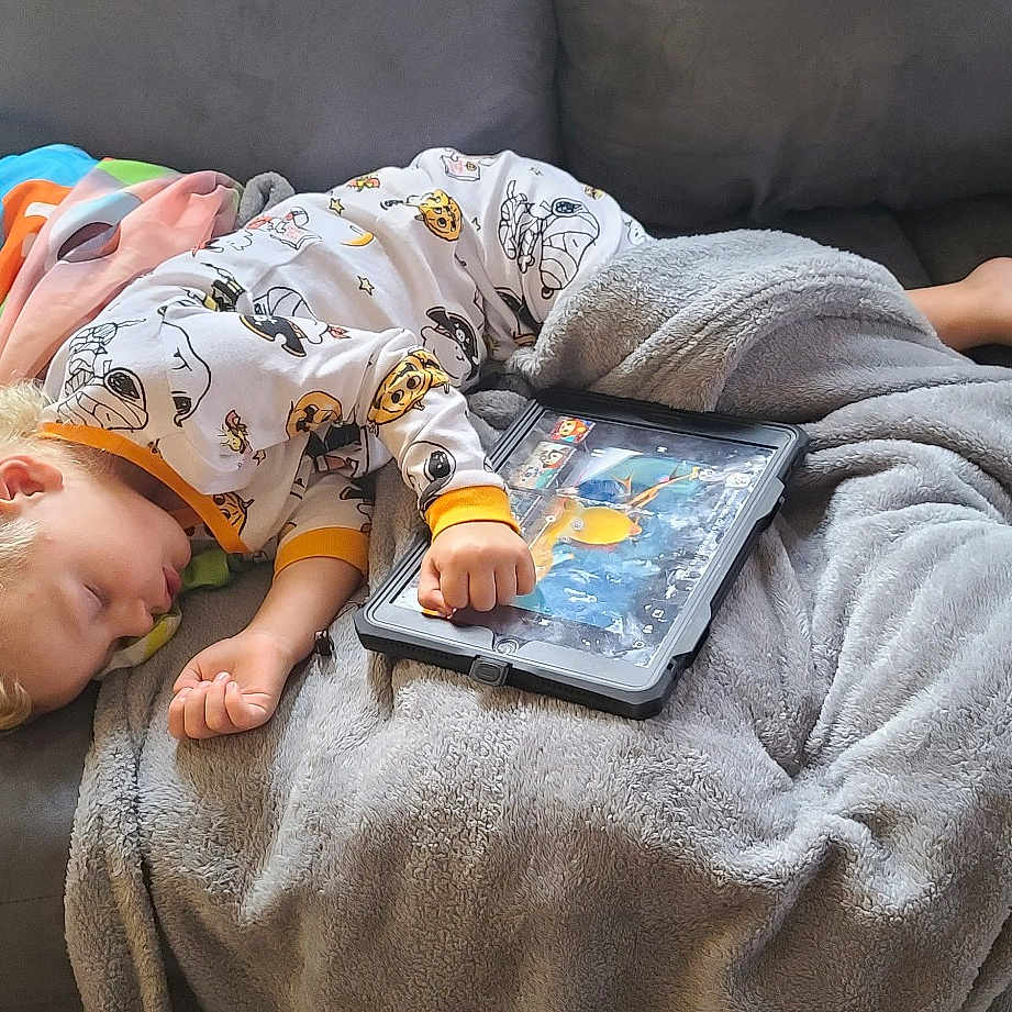 Gunner is registered to the contest to win money with this photo: baby, bedtime, child, comfort, couch, flooring, fun, grass, green, grey, happy, human_body, leisure, linens, nap, room, sitting, textile, toddler, tree