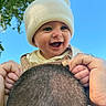Gabriel is registered to the contest to win money with this photo: baby, child, infant, smiling, happy, portrait, outdoor, sky, blue_sky, trees, leaves, hat, beanie, clothing, overalls, adult, shoulders, family, closeup, photography