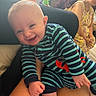 baby, smiling, striped_clothing, indoor, person, adult, woman, seated, family, joyful, playful, onesie, hand, skin, face, happy, couch, window, plant, home
