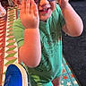 toddler, child, sunglasses, green_romper, dinosaur_print, smiling, indoor, colorful_floor, star_pattern, blue_sneaker, adult, people, casual_clothing, footwear, playful, happy, short_hair, standing, person, family